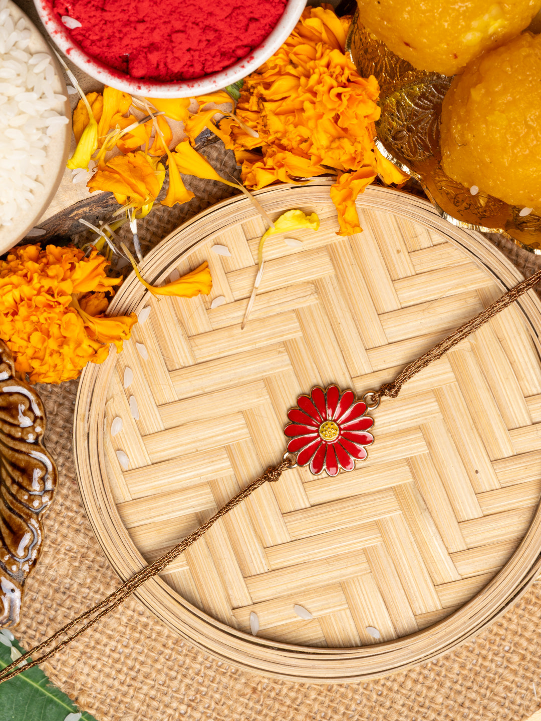 LOOK AND ADORN floral rakhi with red flower design on woven bamboo plate surrounded by marigold flowers and sweets
