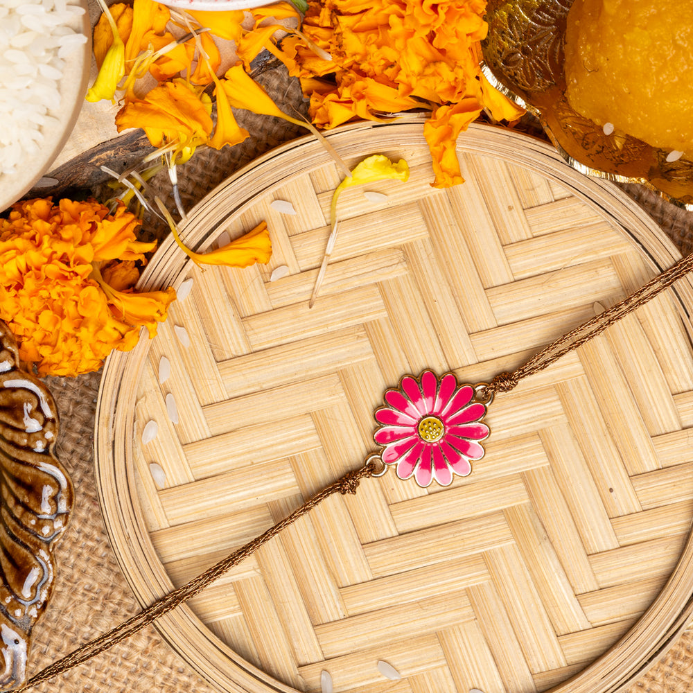 LOOK AND ADORN floral rakhi with pink flower design on woven tray surrounded by marigold flowers and traditional items