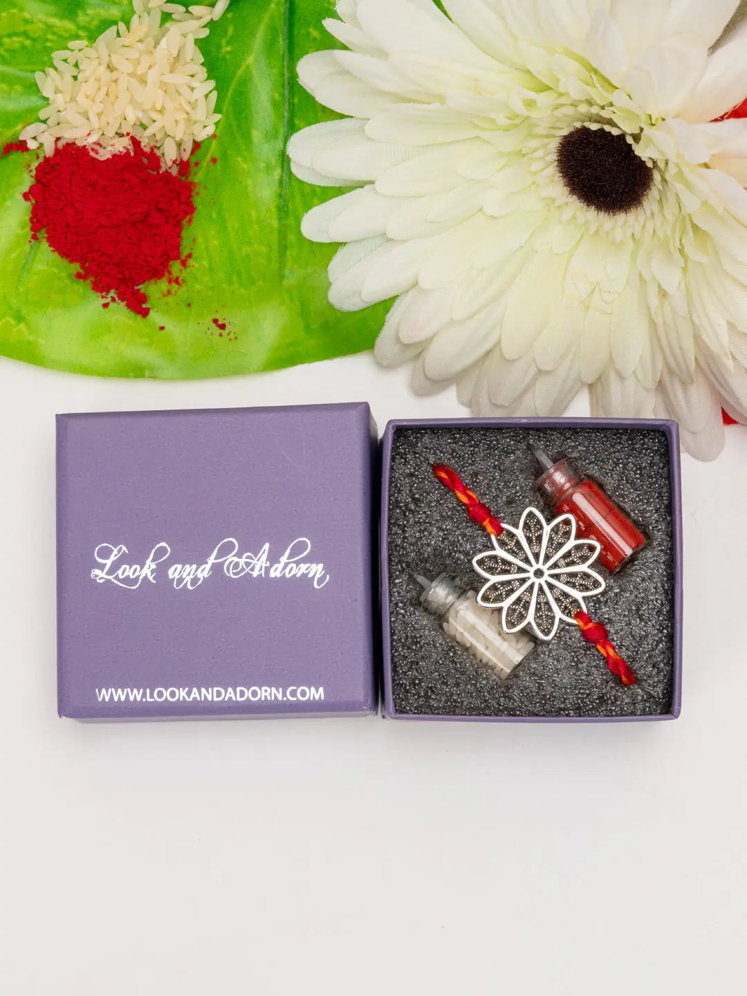 LOOK AND ADORN floral rakhi with decorative flower design in gift box alongside white flower and traditional rice and red powder