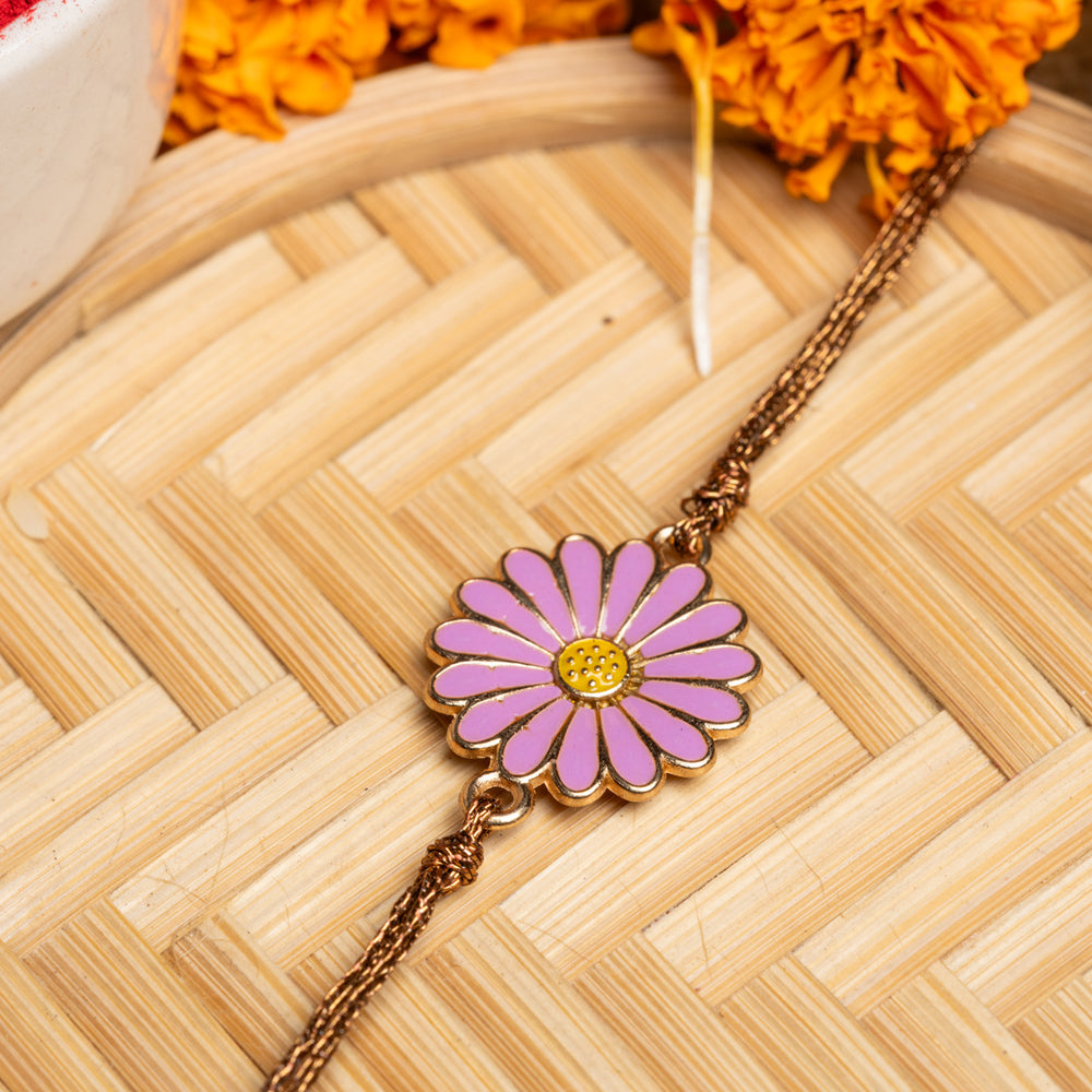 LOOK AND ADORN floral rakhi with pink and yellow flower design on golden chain placed on woven mat