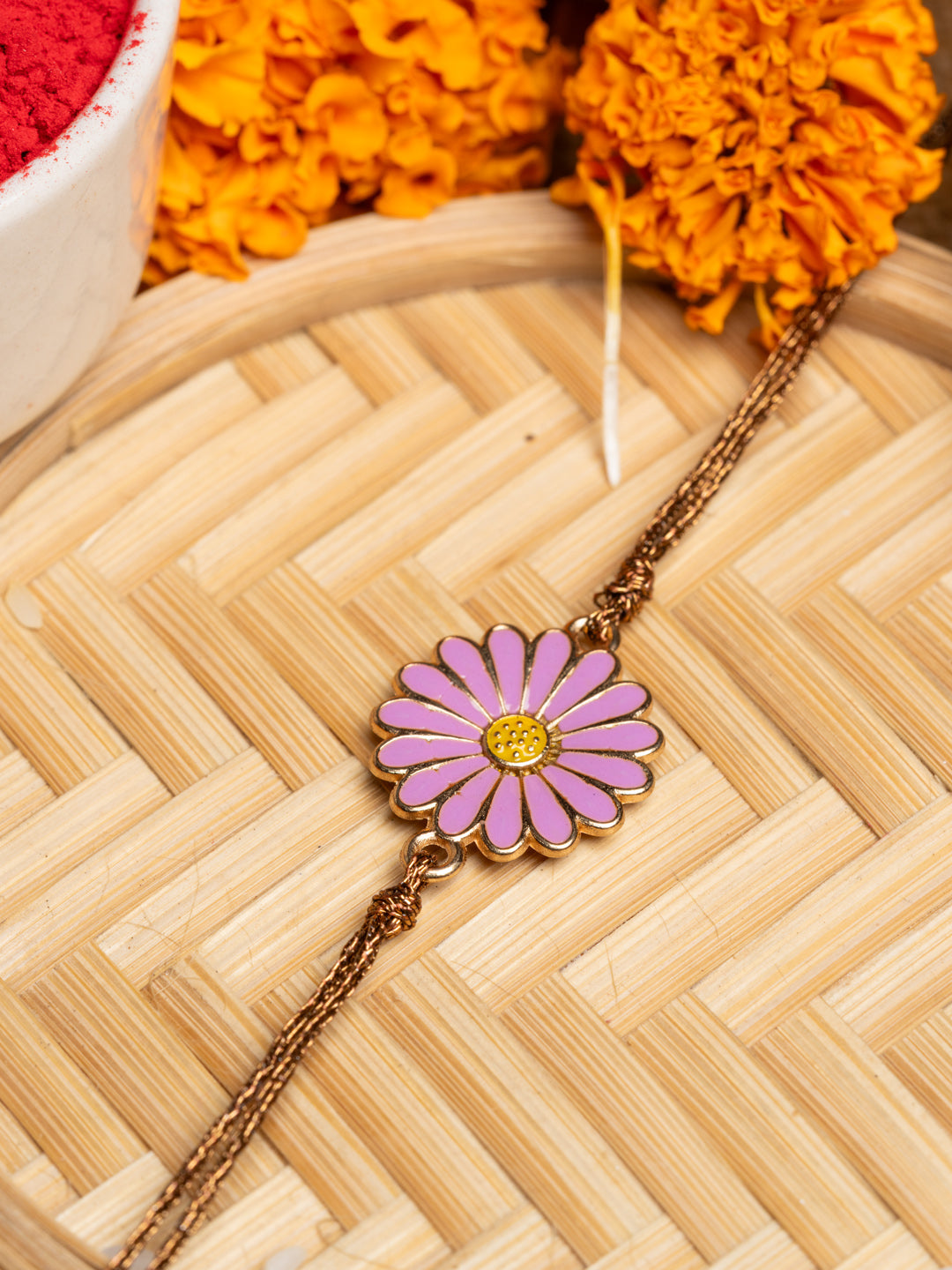 LOOK AND ADORN floral rakhi with pink and yellow flower design on golden chain placed on woven mat