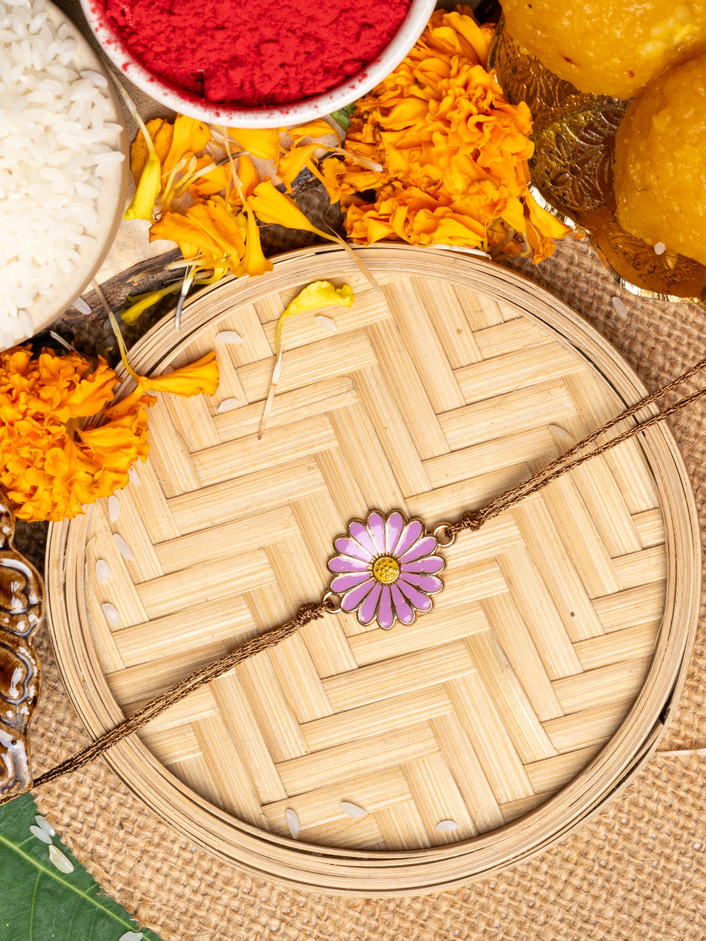 LOOK AND ADORN floral rakhi with purple flower design placed on woven tray with marigold flowers and traditional items