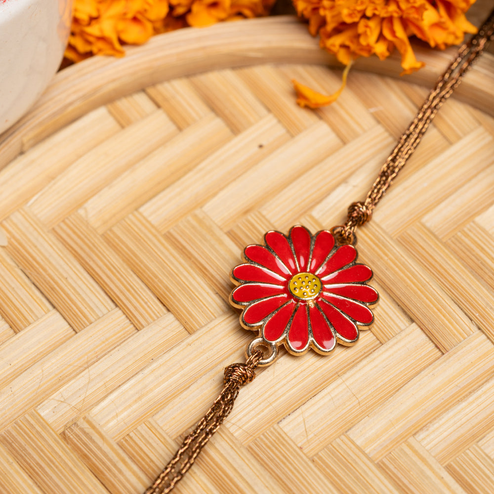 Red floral rakhi with gold chain placed on a woven bamboo mat with marigold flowers in background