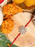 LOOK AND ADORN floral rakhi with silver flower design and red thread on wooden surface with marigold flowers