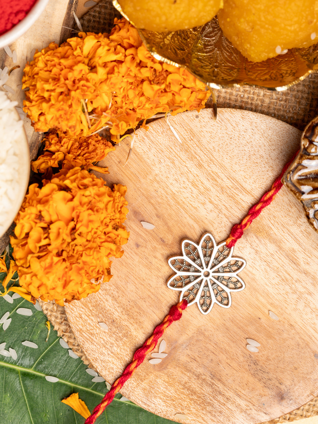 LOOK AND ADORN floral rakhi with silver flower design and red thread on wooden surface with marigold flowers