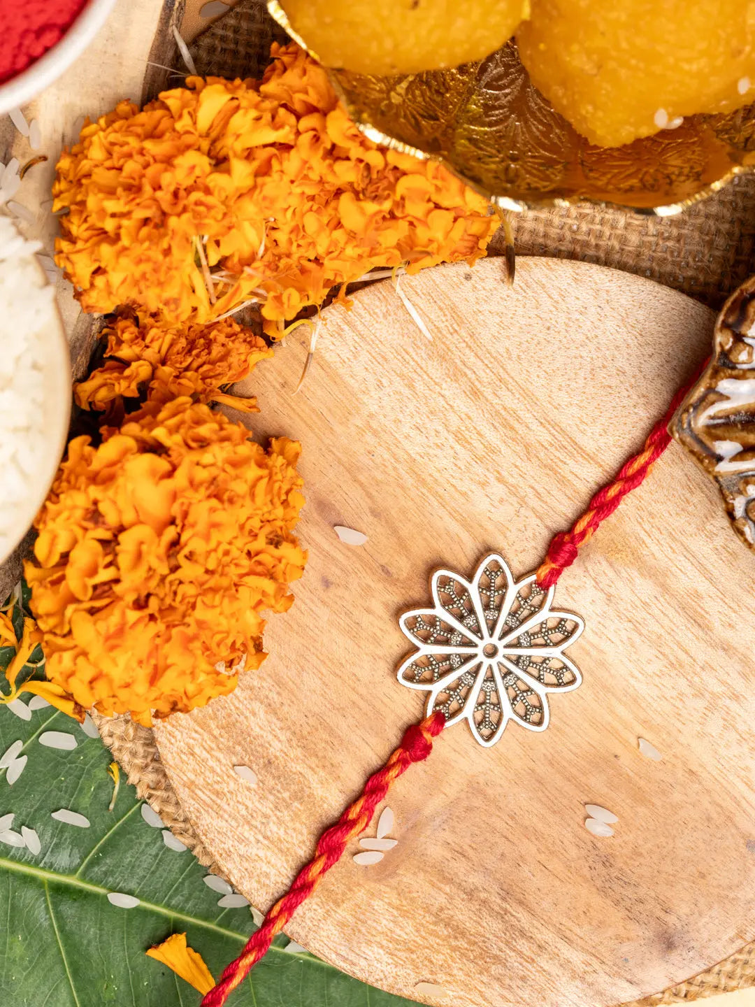 LOOK AND ADORN floral rakhi with silver flower design and red thread on wooden surface with marigold flowers