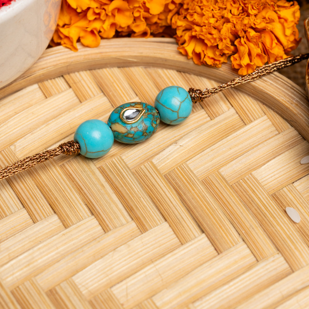 LOOK AND ADORN kundan rakhi with turquoise beads and gold thread on wooden tray with marigold flowers