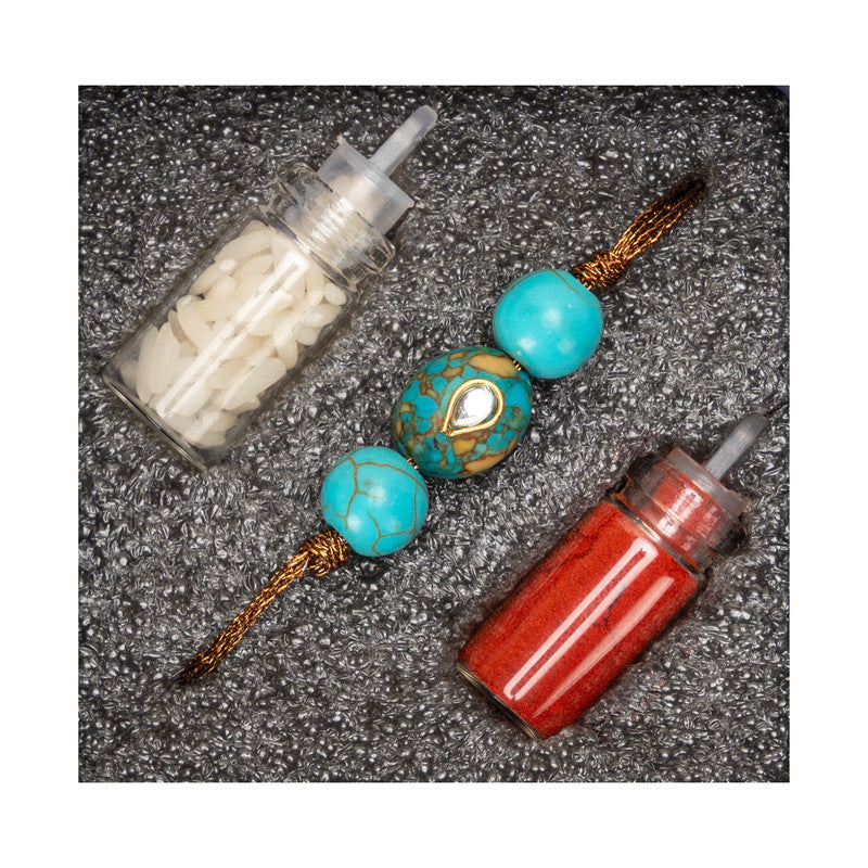 Kundan rakhi with turquoise beads and decorative thread alongside red and white powder containers