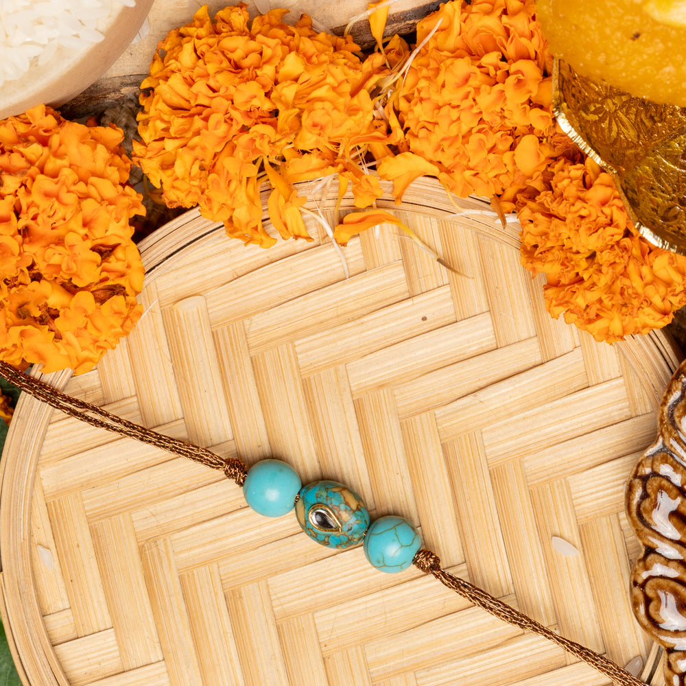 Kundan rakhi with turquoise beads on a woven bamboo tray surrounded by marigold flowers and traditional pooja items