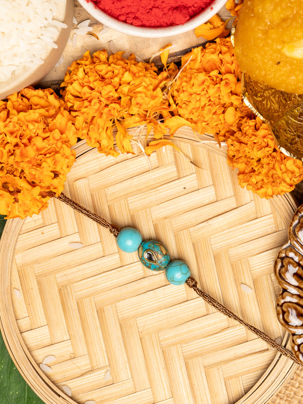 LOOK AND ADORN kundan rakhi with turquoise beads displayed on woven tray with marigold flowers and traditional items