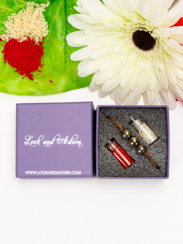 Pyrite rakhi in gift box by LOOK AND ADORN with red and white powder and white flower on green leaf