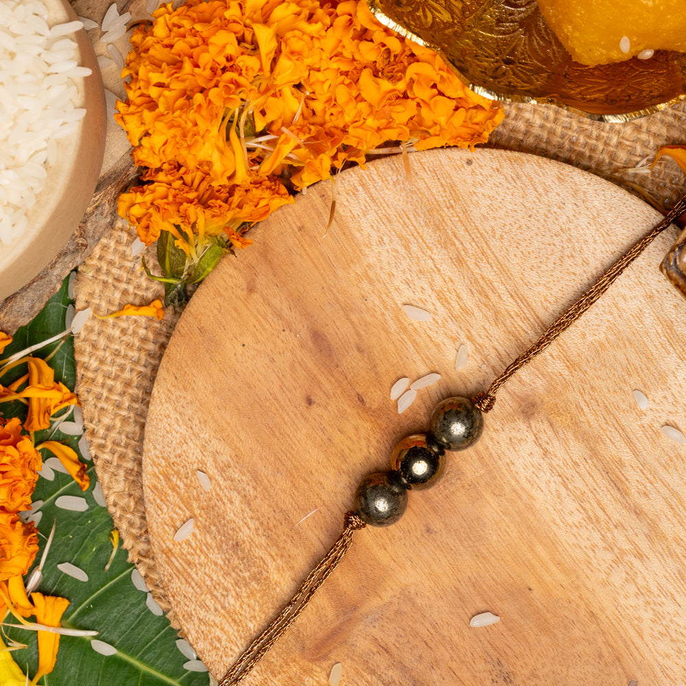 Pyrite rakhi with three metallic beads on golden thread placed on wooden board with marigold flowers and traditional pooja items