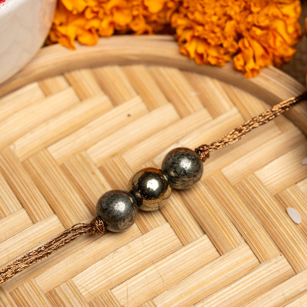 Elegant pyrite rakhi with three metallic beads on a golden thread placed on a woven bamboo tray
