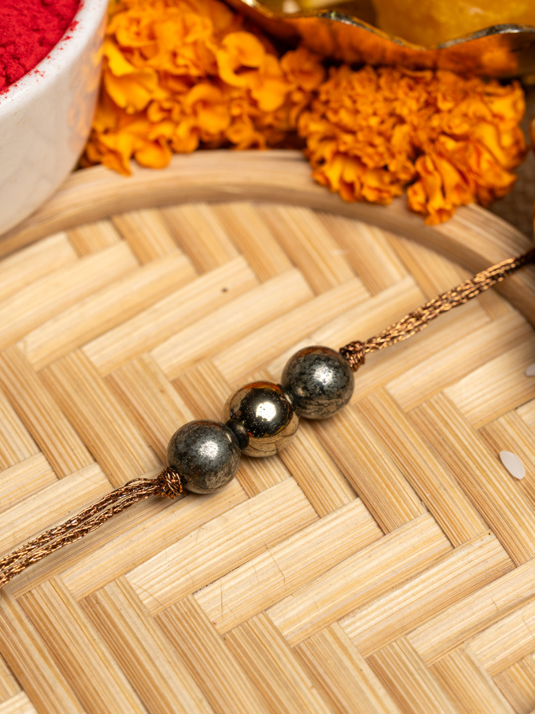 Elegant pyrite rakhi with three metallic beads on a golden thread placed on a woven bamboo tray