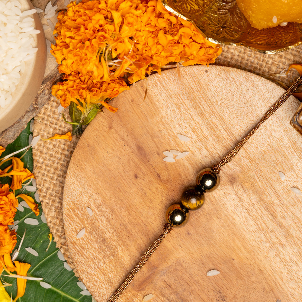 Tiger eye rakhi with polished beads on a wooden plate surrounded by marigold flowers and traditional items