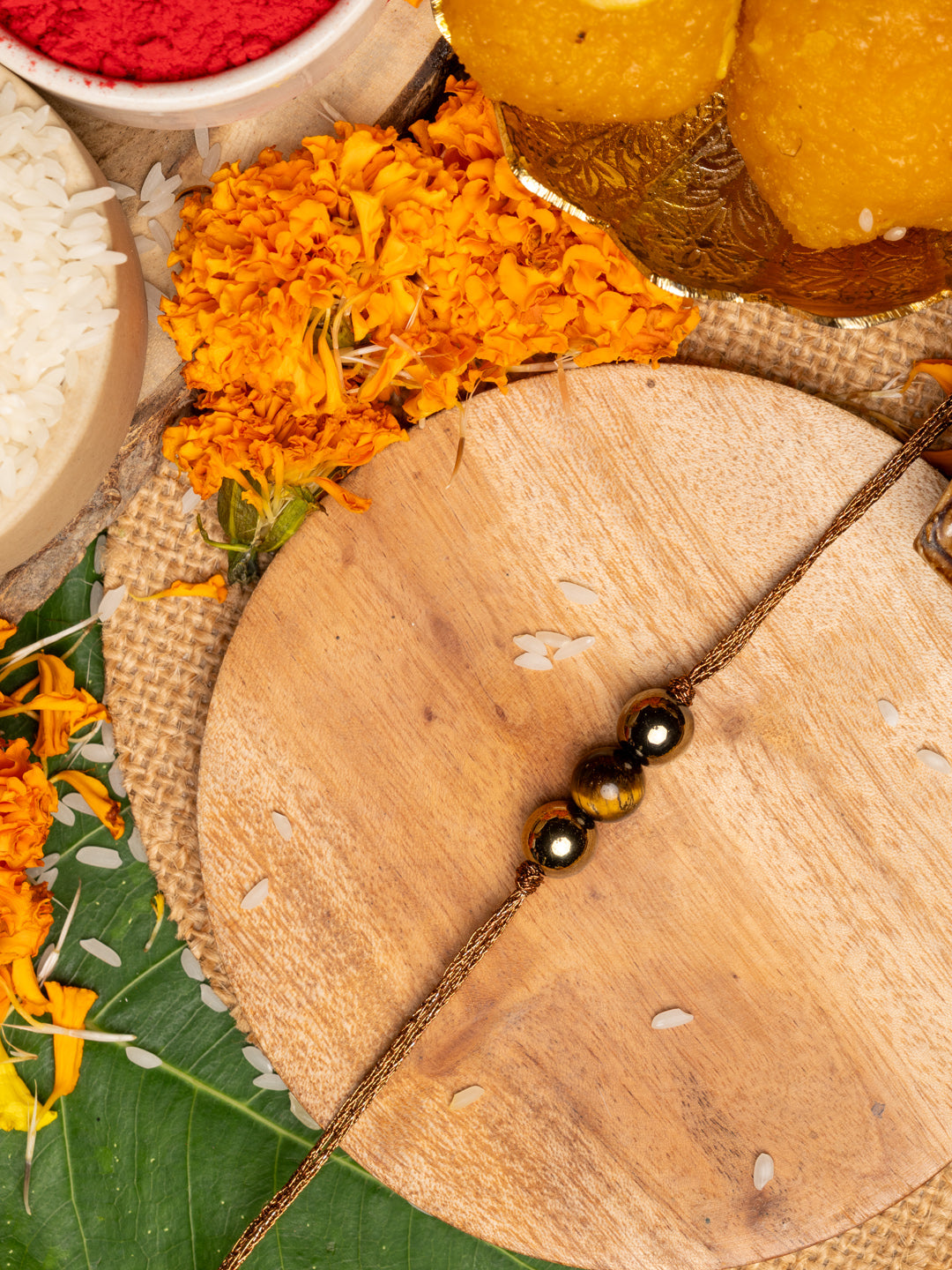 Tiger eye rakhi with polished beads on a wooden plate surrounded by marigold flowers and traditional items