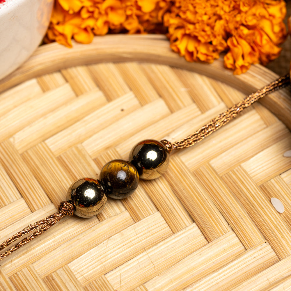 LOOK AND ADORN tiger eye rakhi with polished beads on golden thread and marigold flowers background