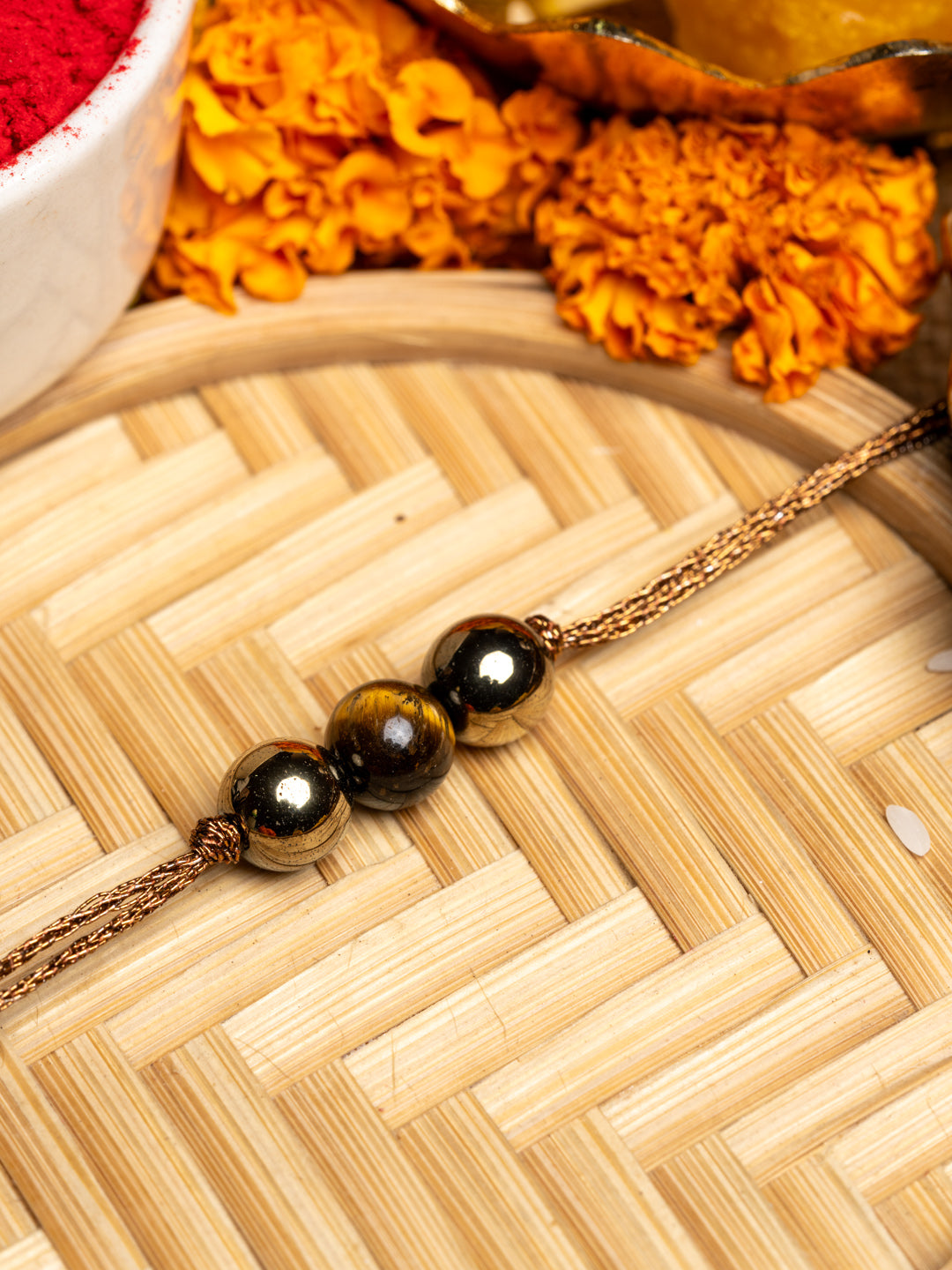 LOOK AND ADORN tiger eye rakhi with polished beads on golden thread and marigold flowers background