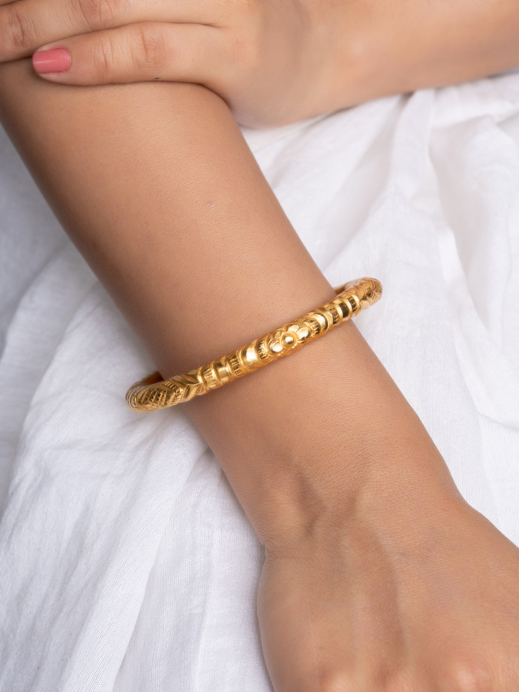 LOOK AND ADORN gold plated bangle with detailed carved texture on wrist against white fabric