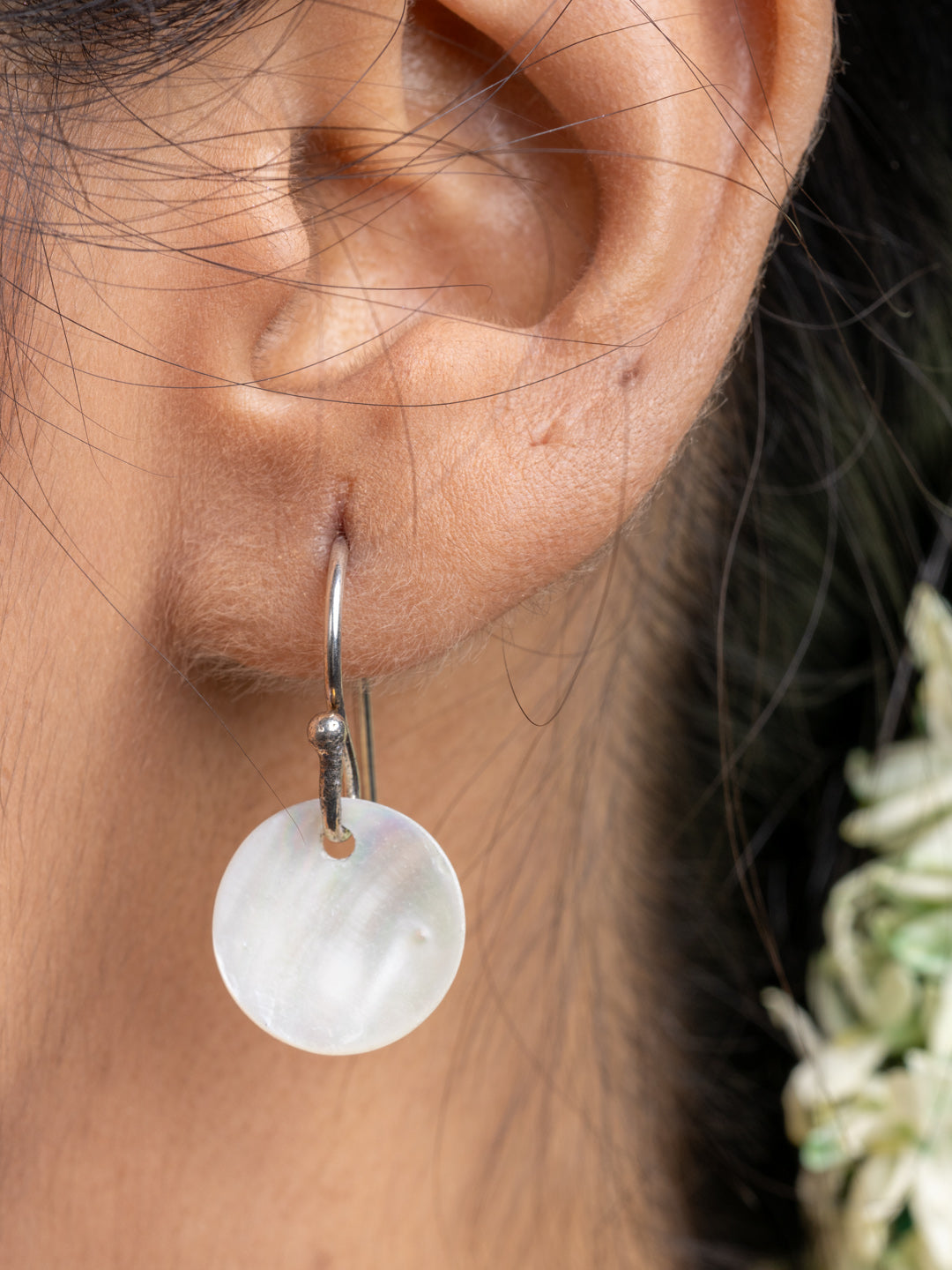 Close-up of a silver hoop earring with a round mother of pearl pendant from a mother of pearl necklace set