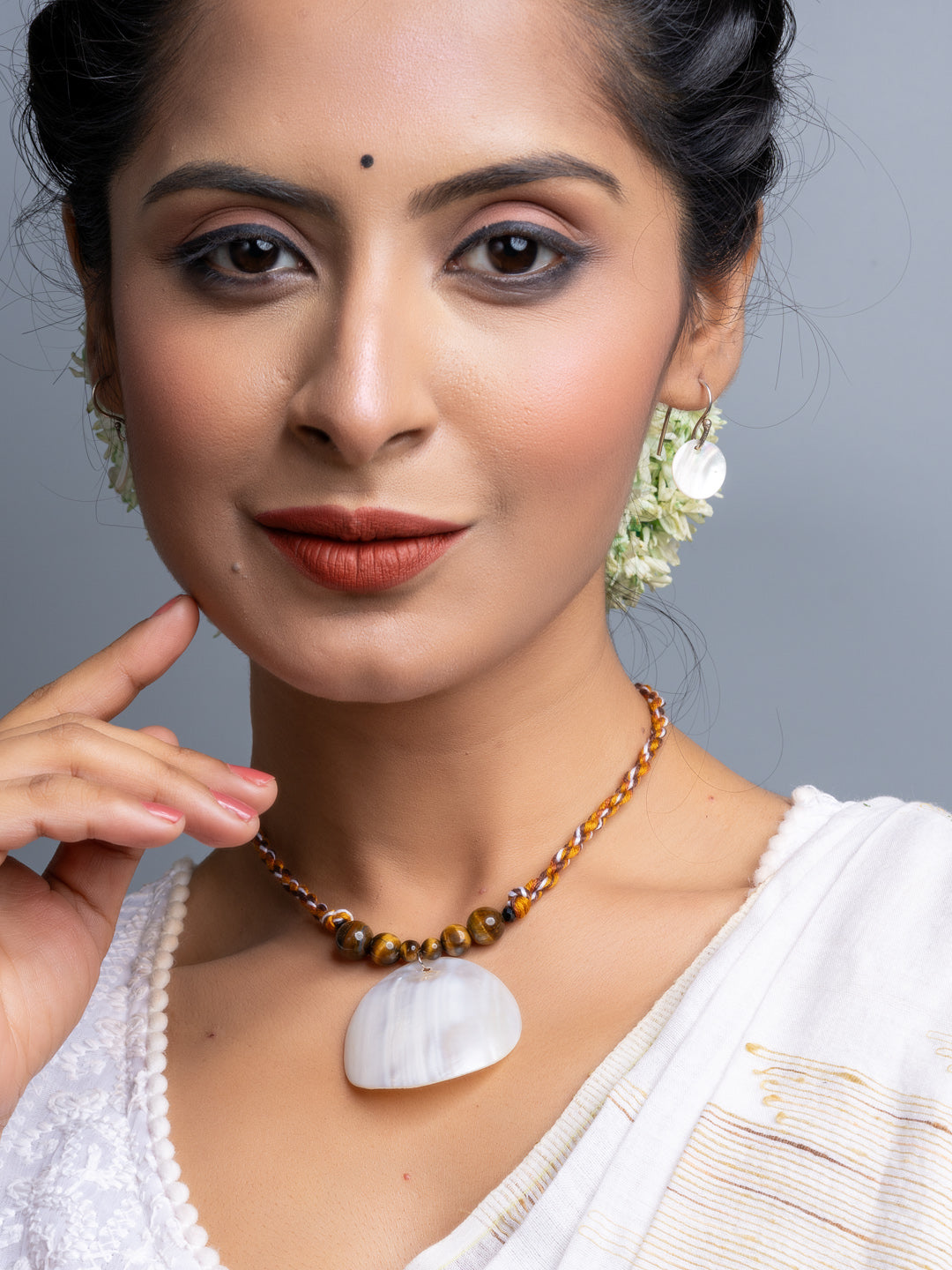 Handmade mother of pearl necklace set with brown beaded chain worn by woman in white attire