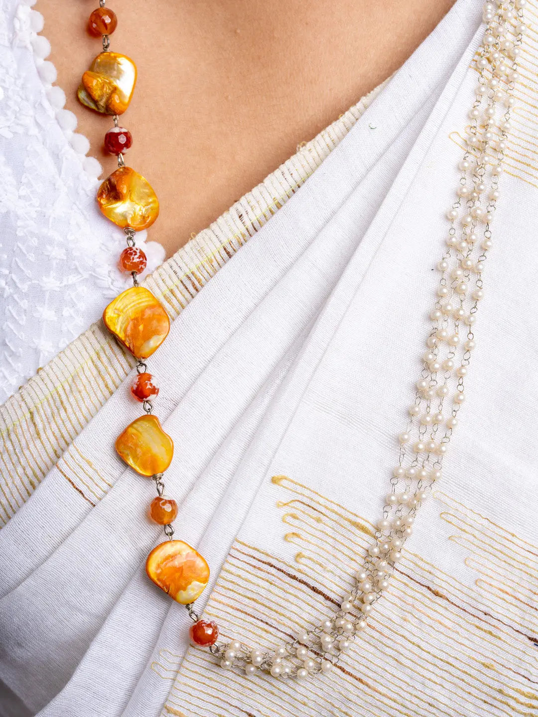Handmade mother of pearl necklace set featuring golden and white beads on a white embroidered fabric