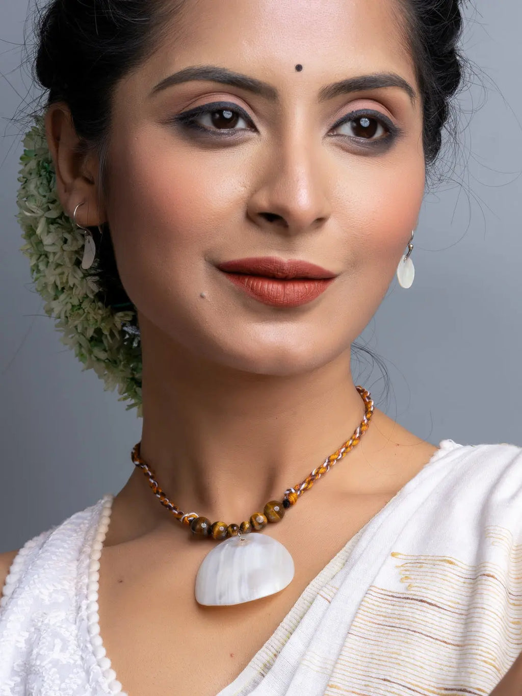 Woman wearing a handmade mother of pearl necklace set with a white shell pendant and matching earrings