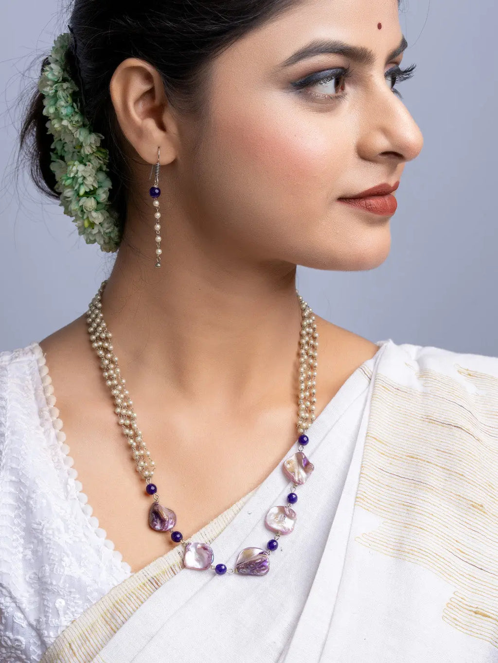 Handmade mother of pearl necklace set featuring purple beads worn by woman in traditional white saree