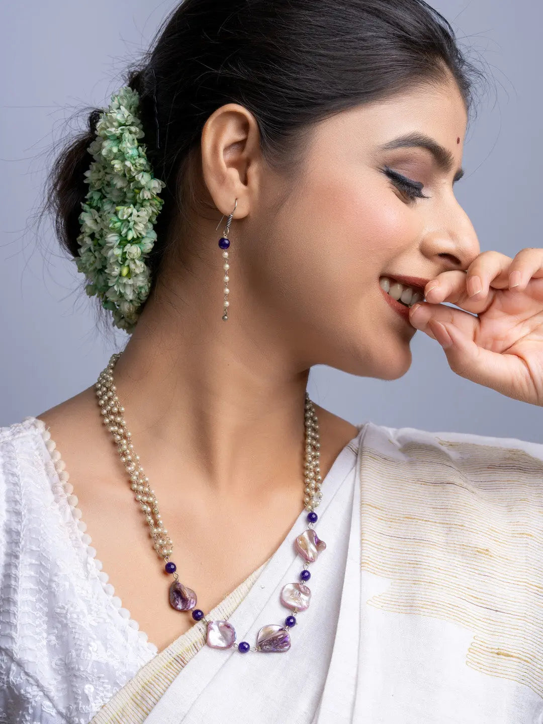Woman wearing a handmade mother of pearl necklace set with purple and white beads and matching earrings