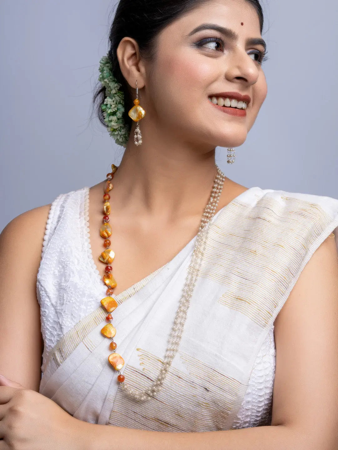 Woman wearing handmade mother of pearl necklace set with golden and orange beads paired with traditional white saree