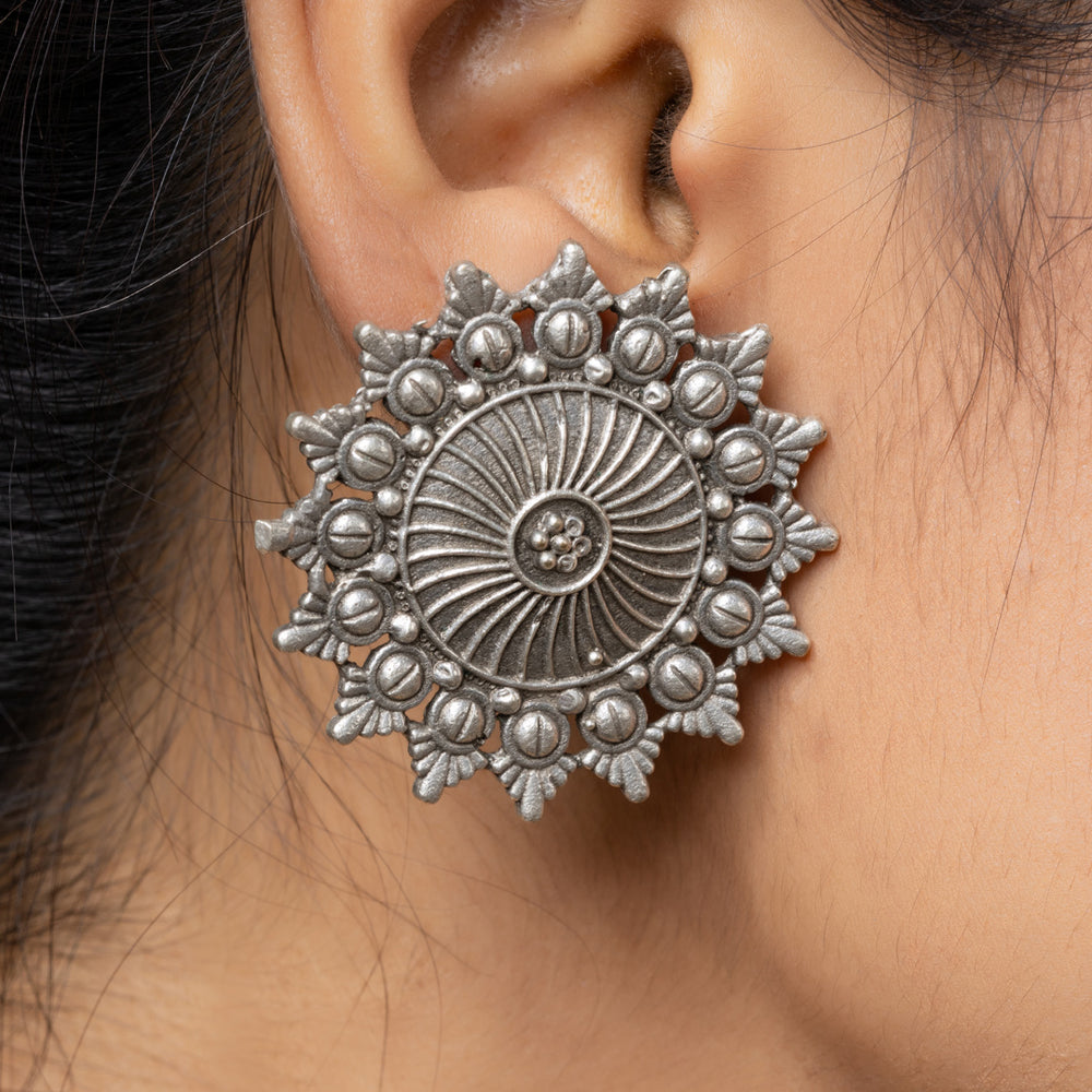 Close-up of a woman's ear wearing detailed oxidised earrings in a floral circular design