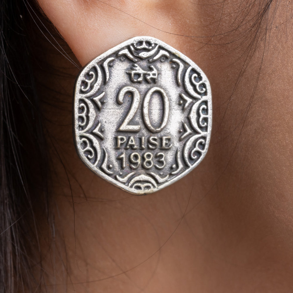 Close-up of oxidised silver earrings shaped like a 20 paise coin worn on ear