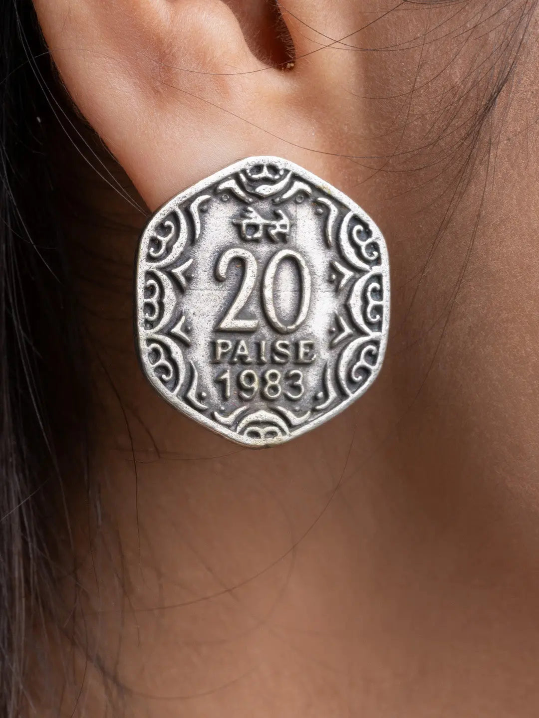 Close-up of oxidised silver earrings shaped like a 20 paise coin worn on ear