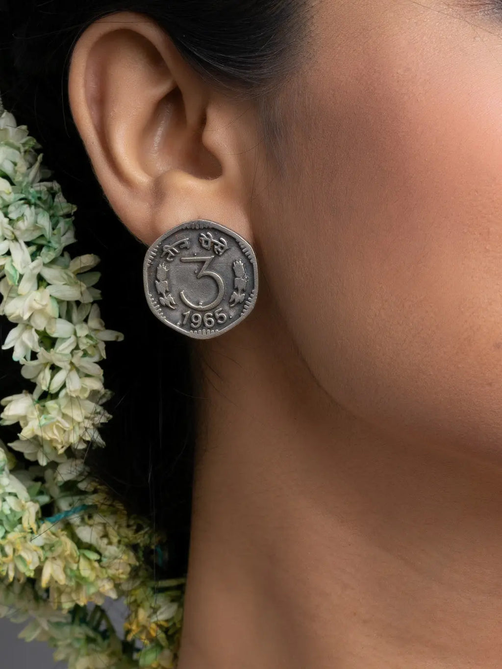 Close-up of oxidised silver earrings designed like vintage coins worn on ear with floral background