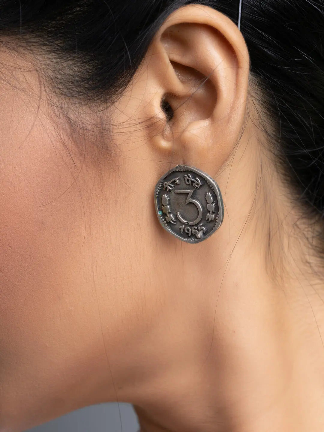 Close-up of a woman's ear wearing oxidised silver earrings with intricate symbols and designs