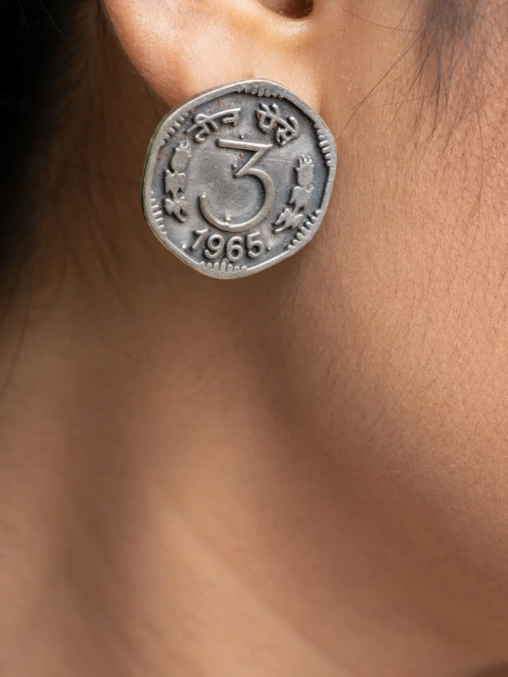 Close-up of oxidised silver earrings designed like vintage coins worn on ear