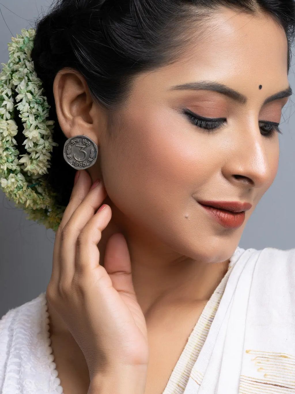 Close-up of woman wearing round oxidised silver earrings with intricate design and floral hair accessory