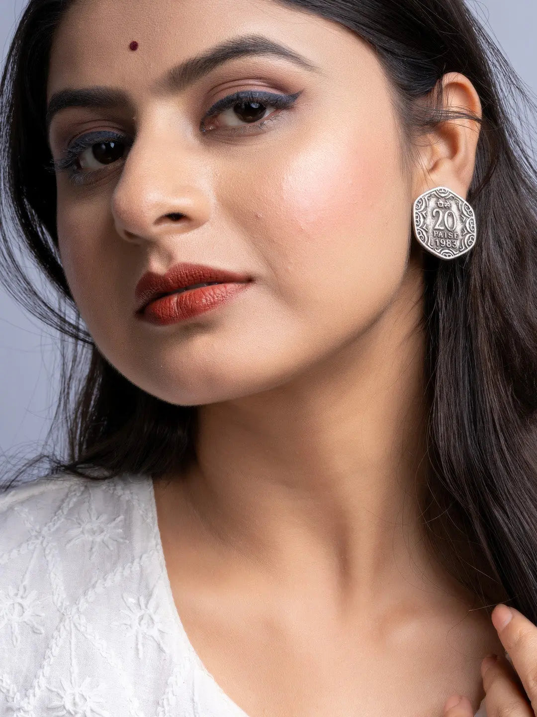 Close-up of woman wearing oxidised silver earrings with intricate vintage coin design