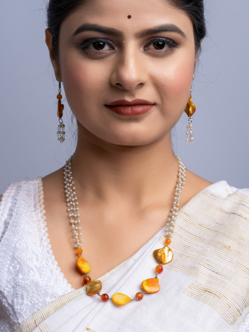 Woman wearing handmade mother of pearl necklace set with white beads and orange accents paired with matching earrings