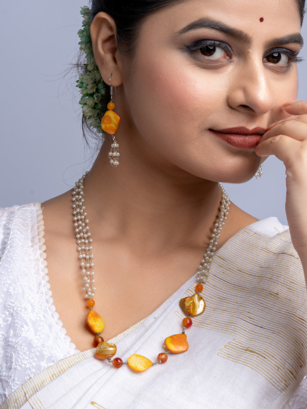 Handmade mother of pearl necklace set with orange and gold beads worn by woman in white saree