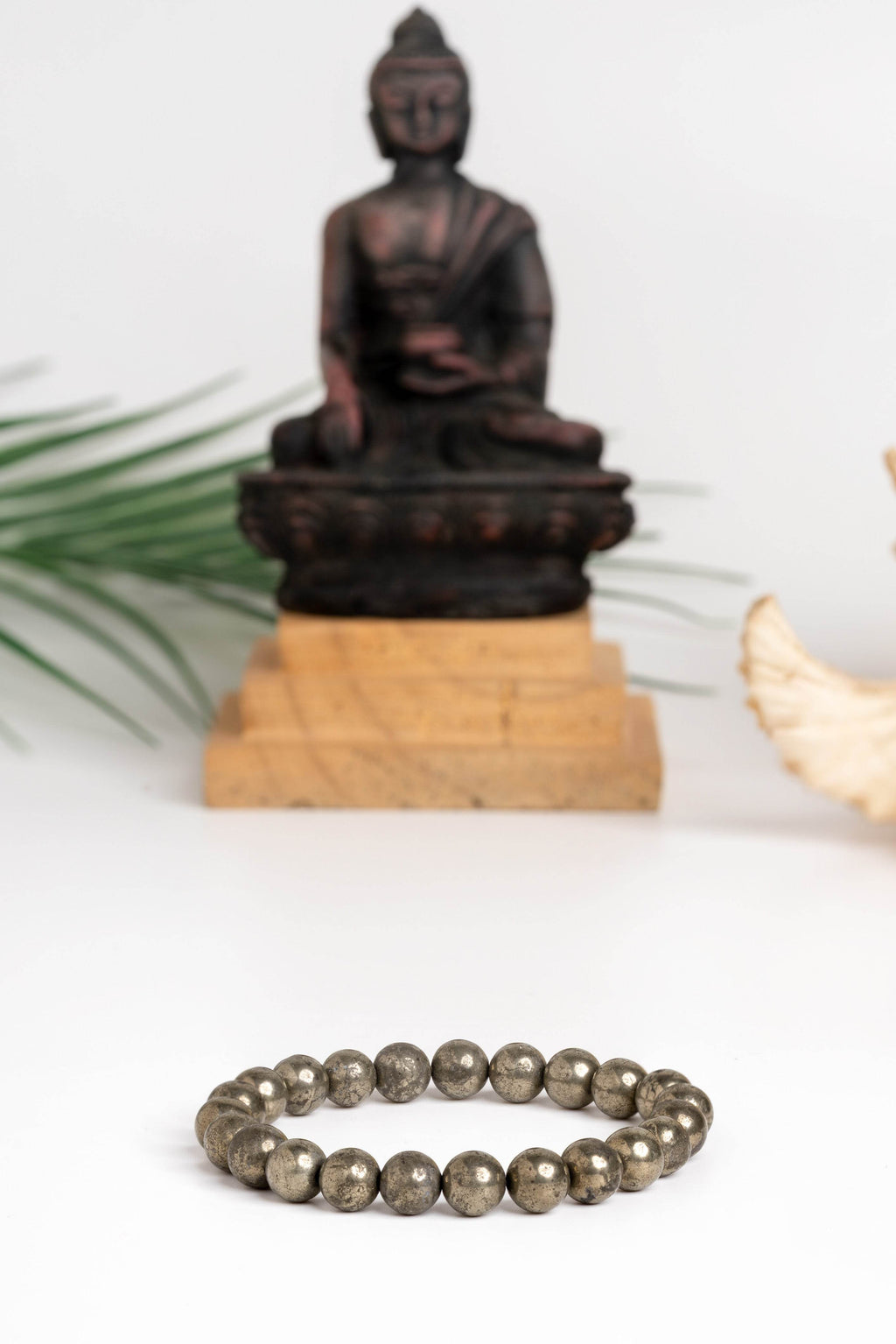 Raw pyrite bracelet made of smooth beads, set against a serene Buddha statue background