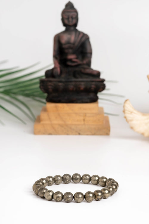 Raw pyrite bracelet made of smooth beads, set against a serene Buddha statue background