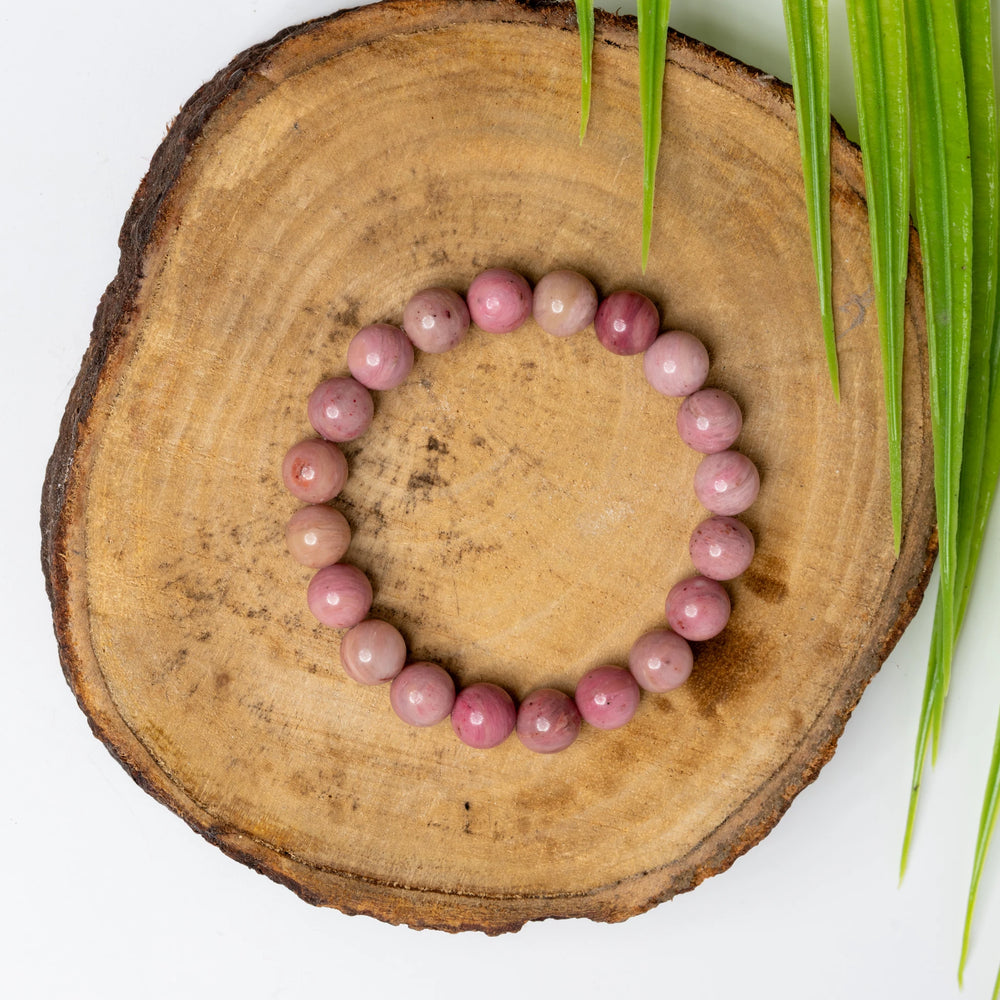 Rhodochrosite bracelet on a wooden slice showcasing its pink and rosy hues for elegant adornment