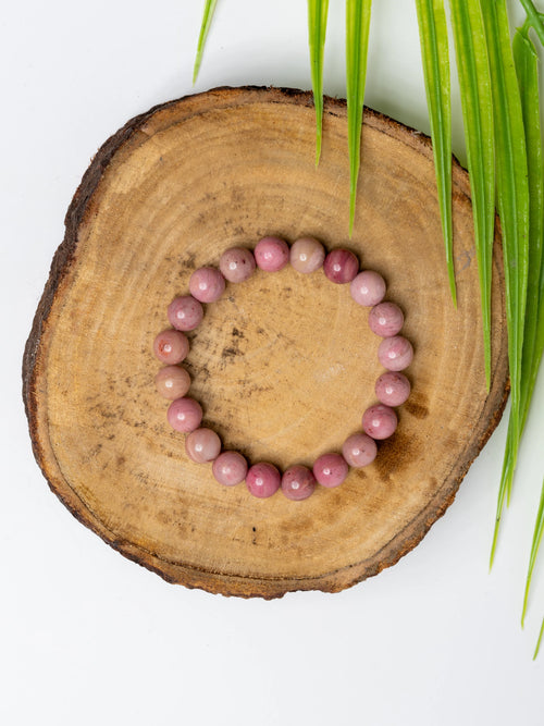 Rhodochrosite bracelet on a wooden slice showcasing its pink and rosy hues for elegant adornment