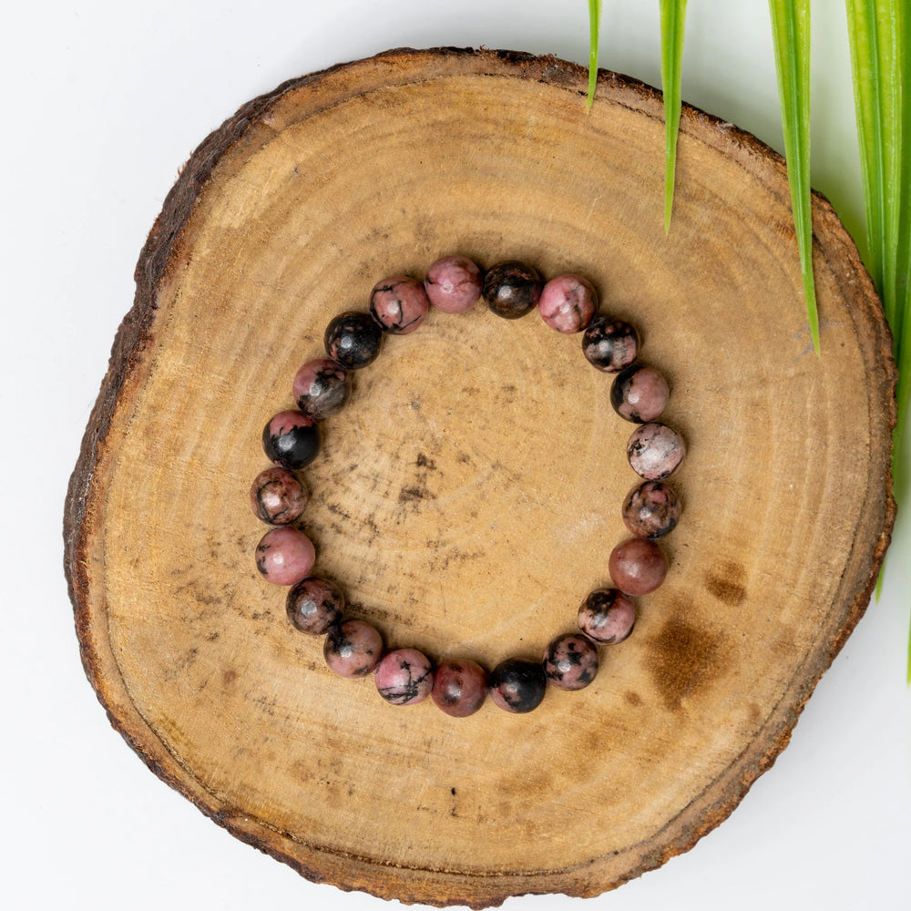 Stunning rhodonite bracelet made with polished beads on a rustic wooden slice background