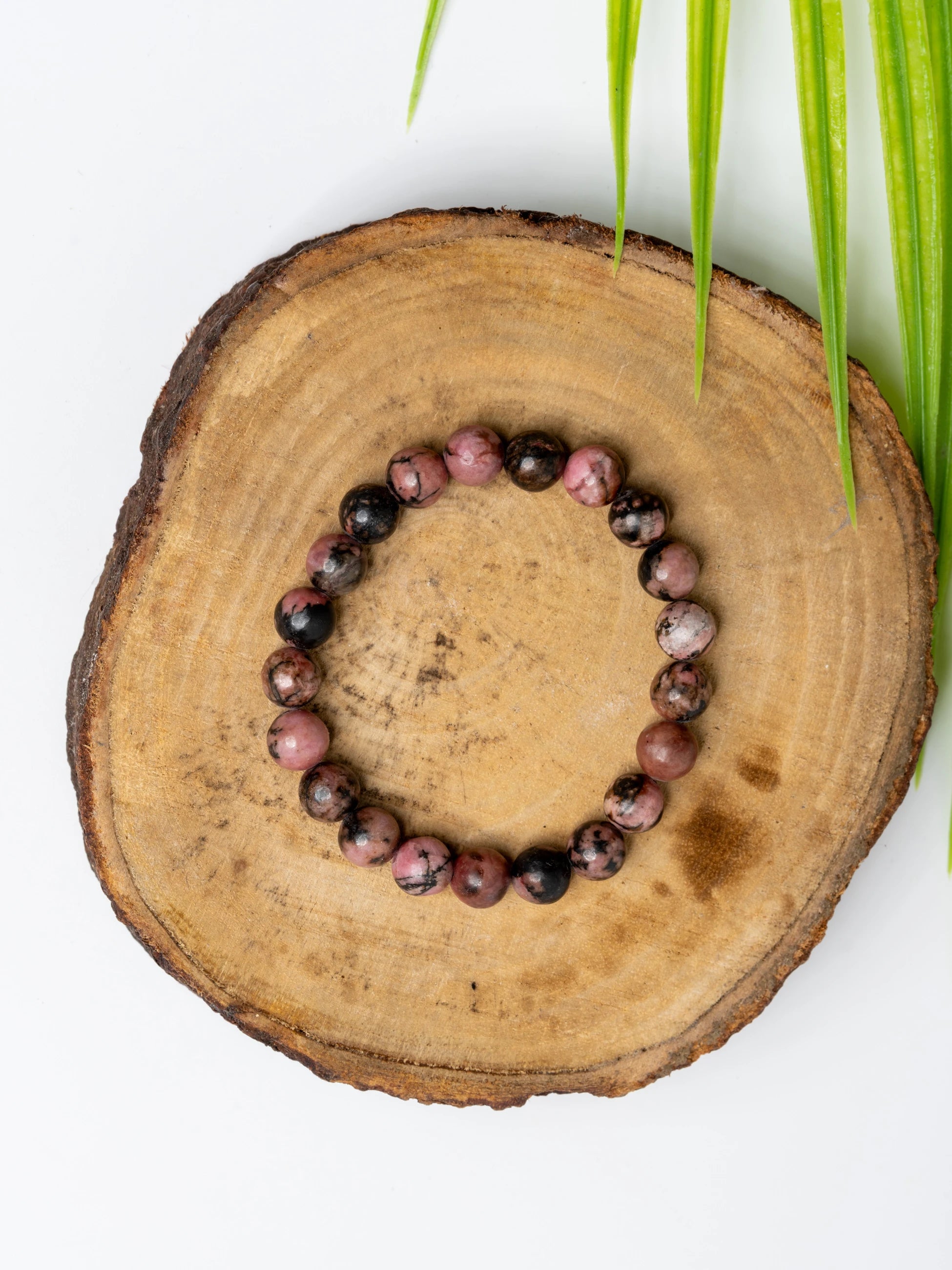 Stunning rhodonite bracelet made with polished beads on a rustic wooden slice background