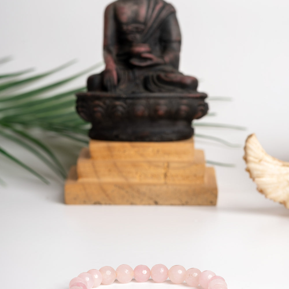 Rose quartz stone bracelet on display with a Buddha statue in the background