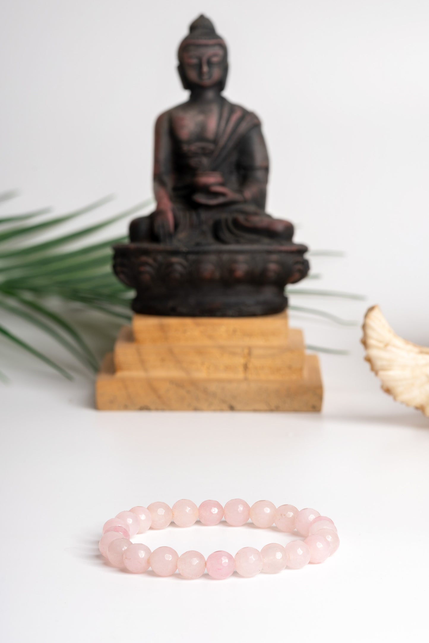 Rose quartz stone bracelet on display with a Buddha statue in the background