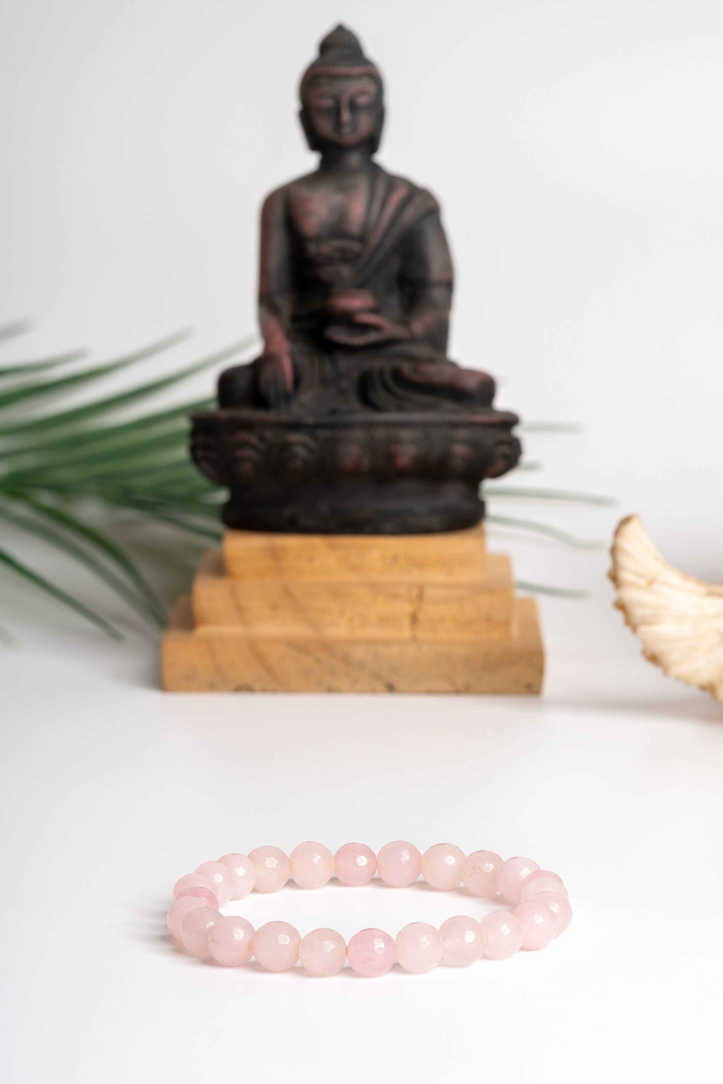 Elegant rose quartz stone bracelet displayed in front of a Buddha statue for a serene look