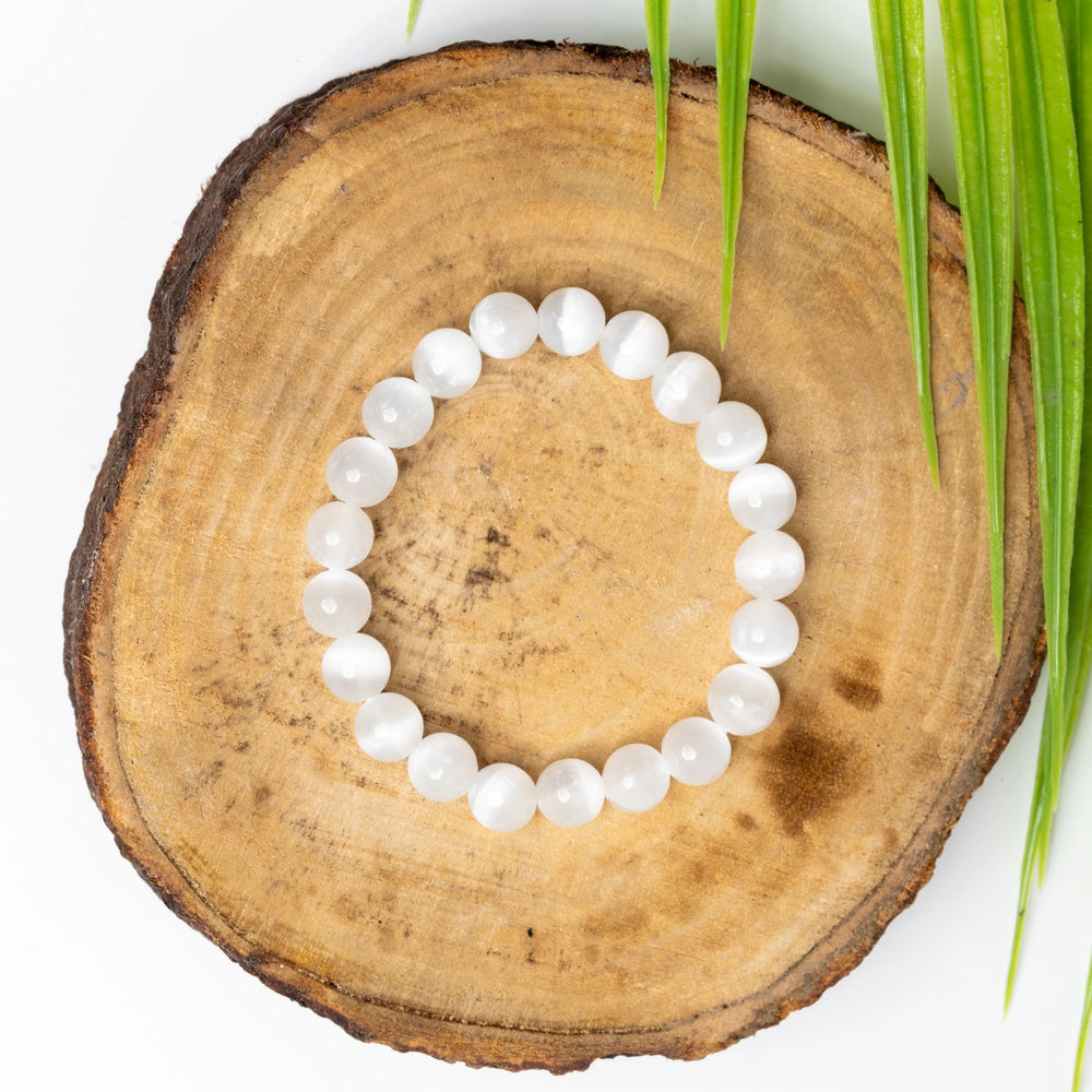 Selenite bracelet made of smooth, polished beads on a wooden surface with green leaves